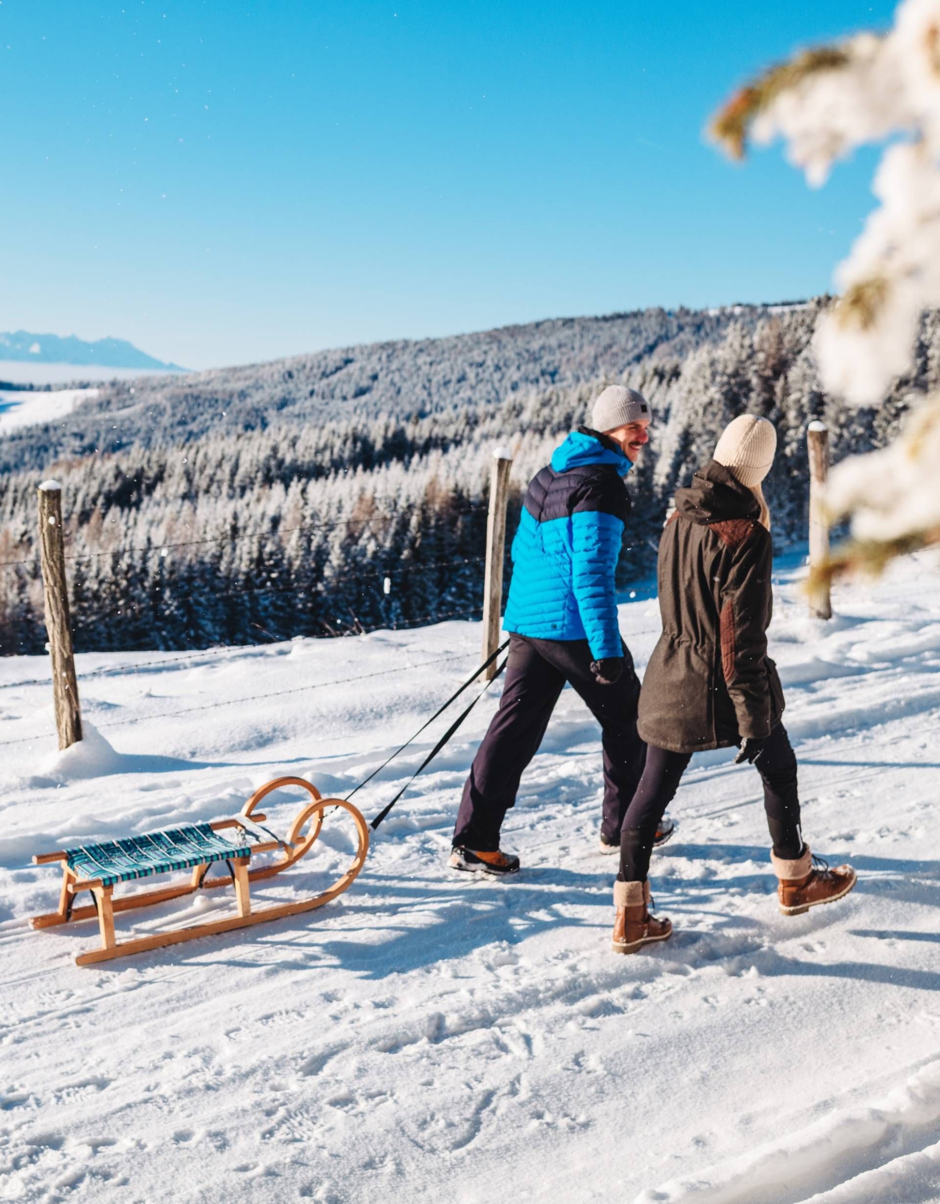 Zwei Personen ziehen ihre Rodel durch eine winterliche Landschaft auf der Saualpe