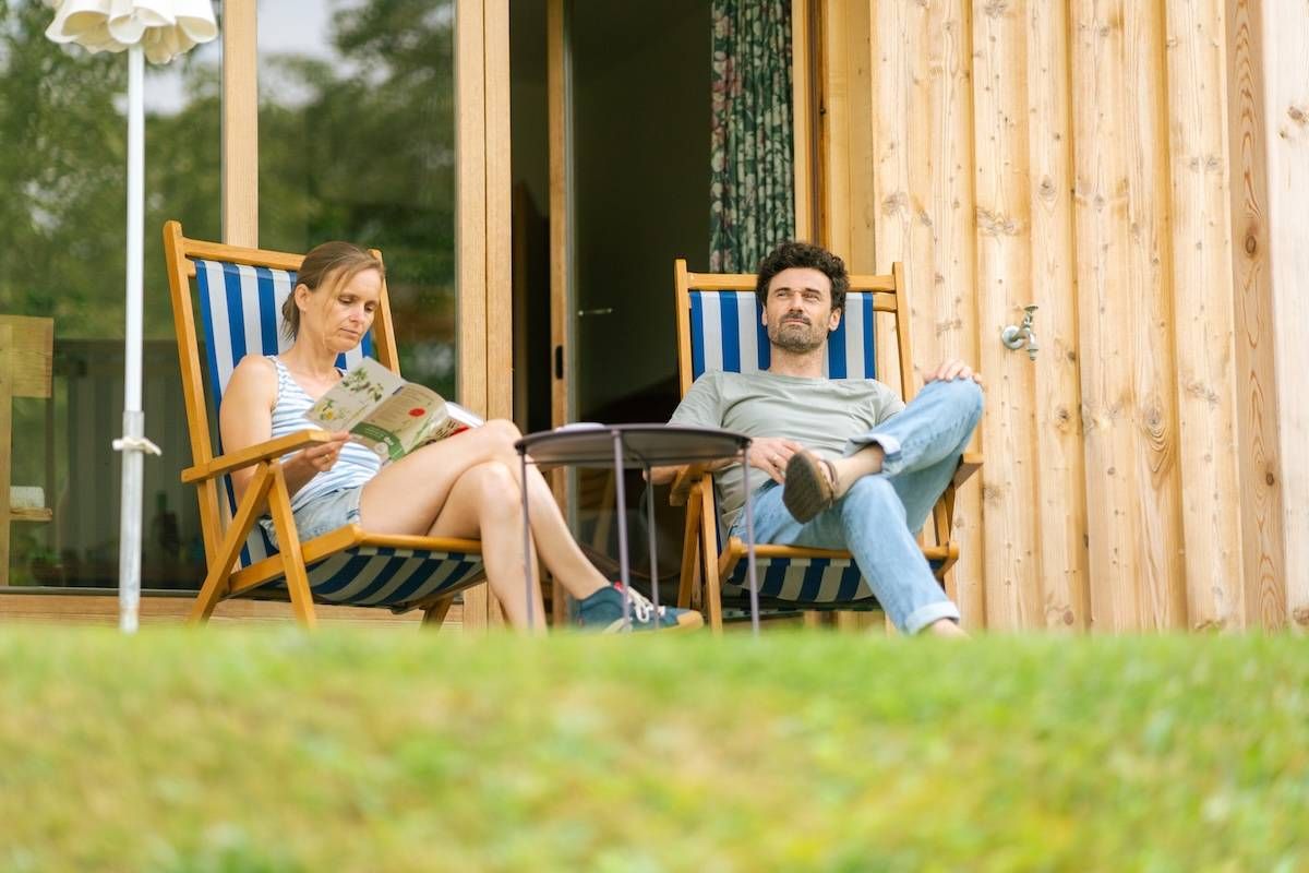 Zwei Personen sitzen auf Sonnenstühlen und die Frau liest ein Buch und der Mann trinkt einen Kaffee
